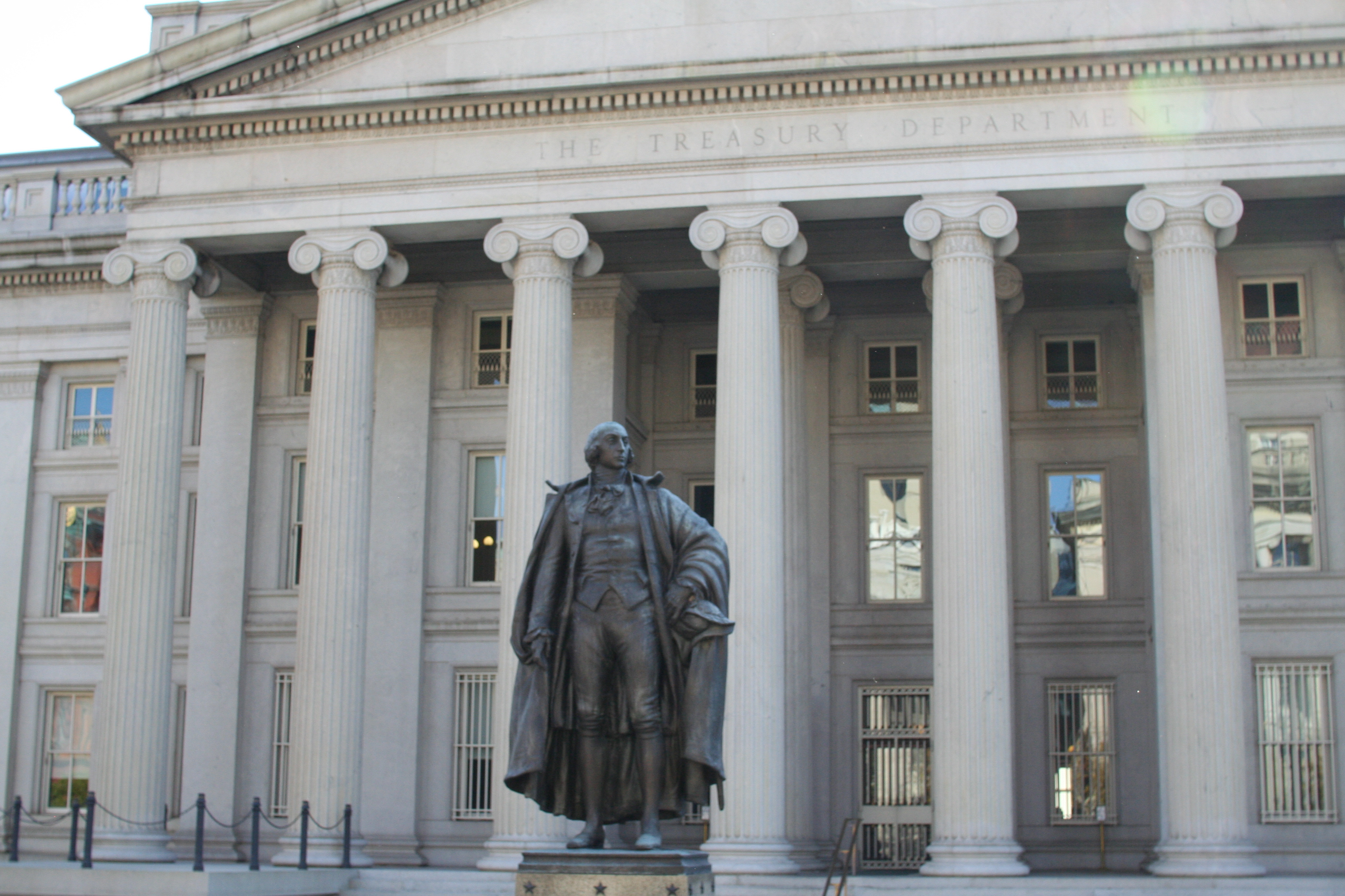 Front of the Treasury Department, Washington DC, with a statue of a man in founding-fathers period dress.