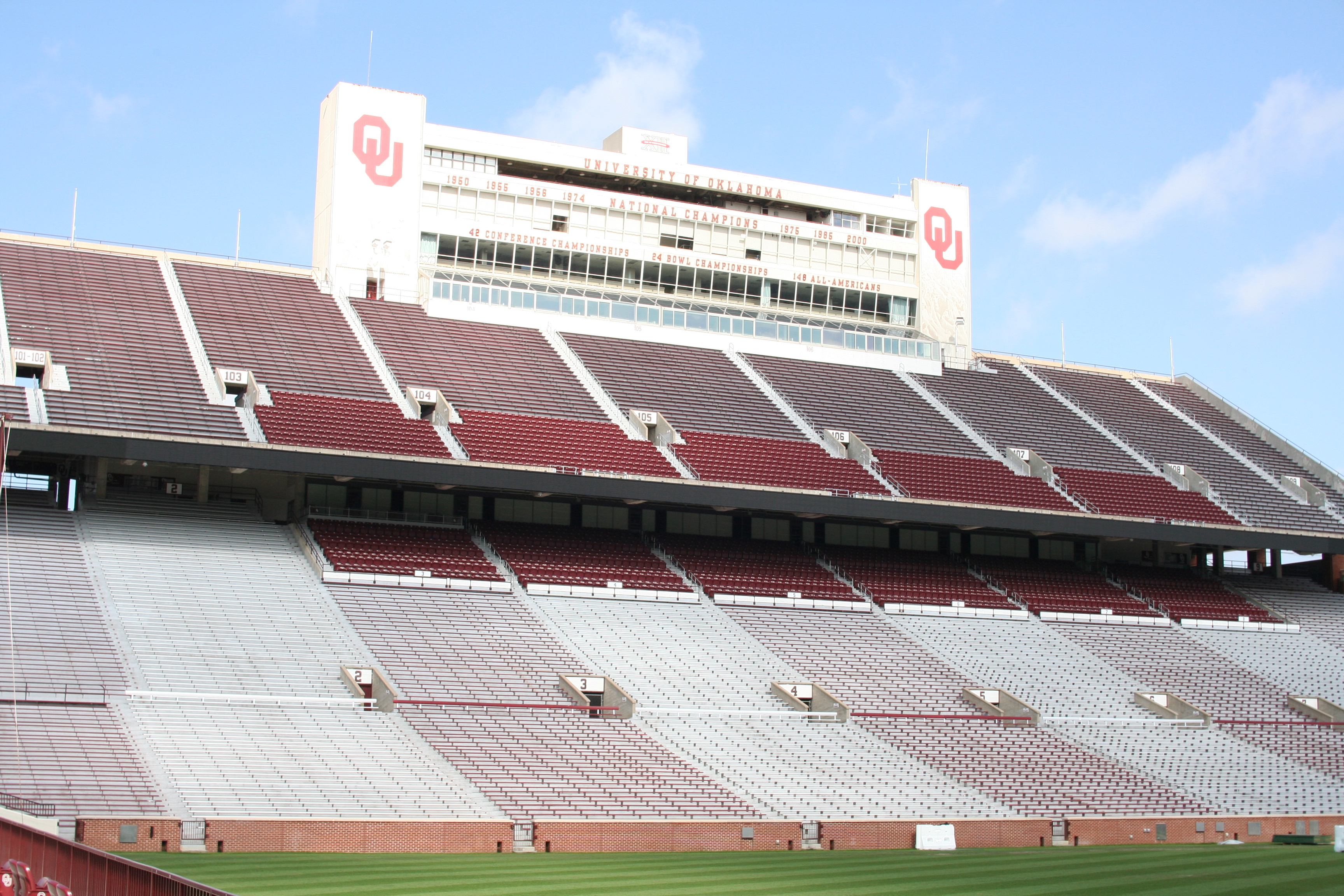 Interior of OU football stadium in daytime, idle with no persons present, showing a great expanse of seating and media/VIP boxes above